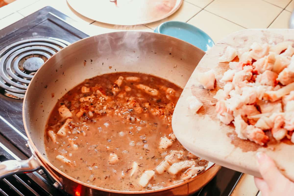 a cutting board with pork belly over a saucier with Hoppin' John ingredients