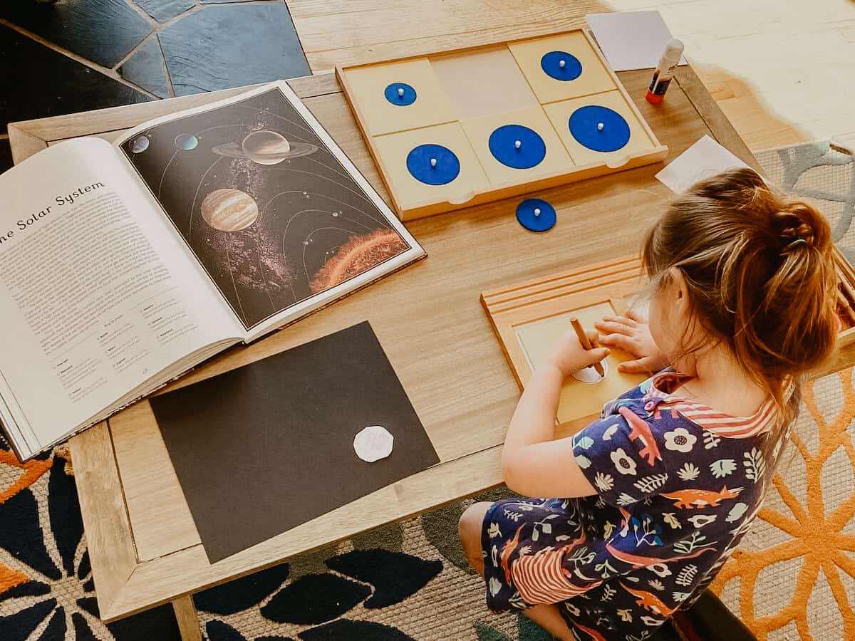 Montessori First Great Lesson Follow-up work: child tracing Geometry Cabinet Circles Drawer and Planetarium book open to The Solar System