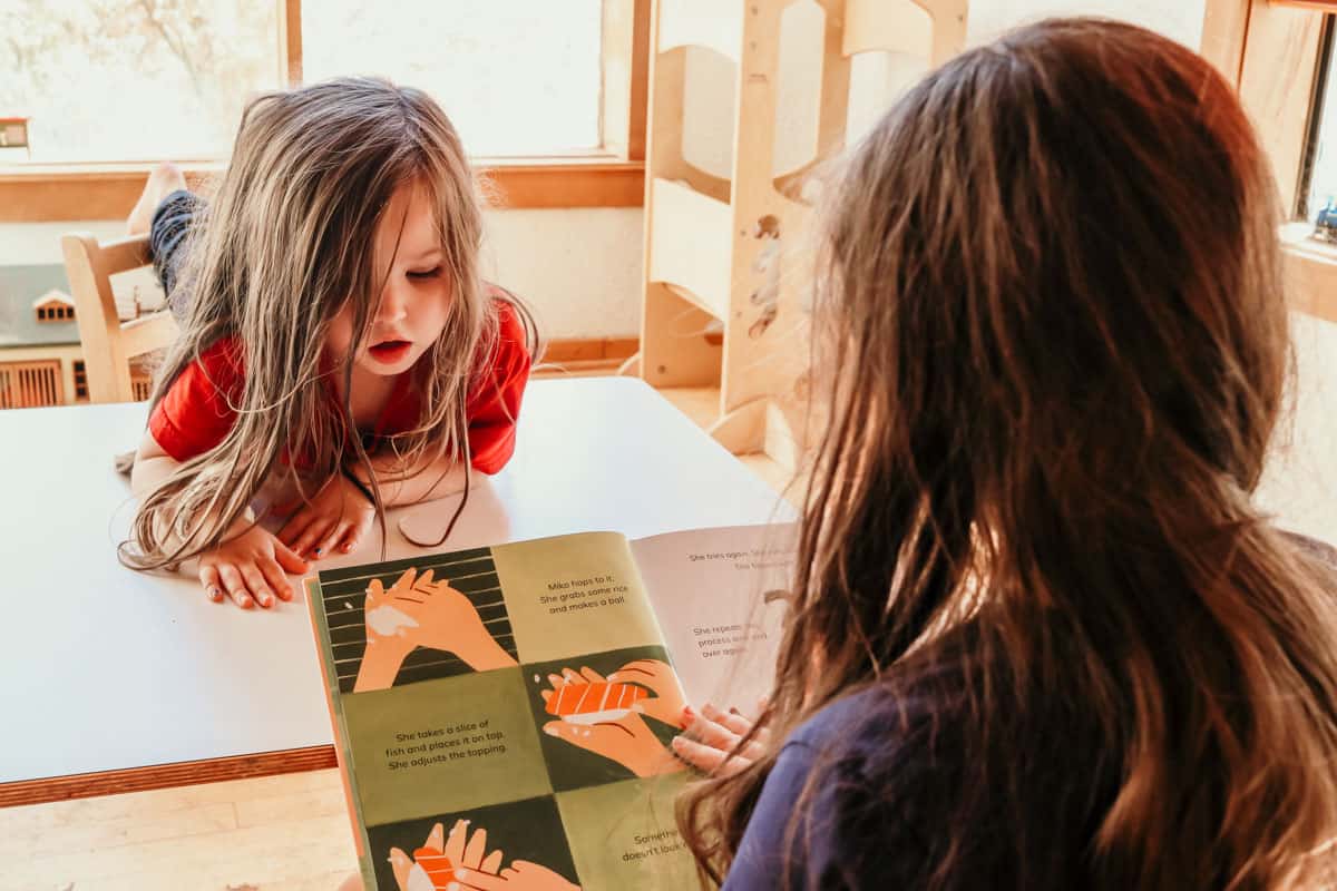 child reading The Perfect Sushi picture book aloud and another child is listening while looking at the pictures